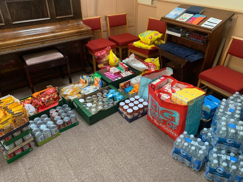 An image of a large donation of food - canned goods, water, squash, cereal - laid out on the floor in a room. 