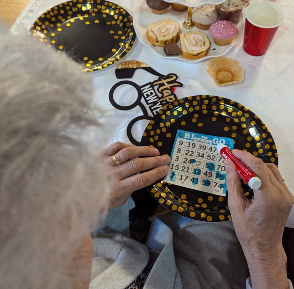 Close-up of hands playing bingo at a New Year’s celebration, with gold-decorated plates, cakes and party decorations on the table.